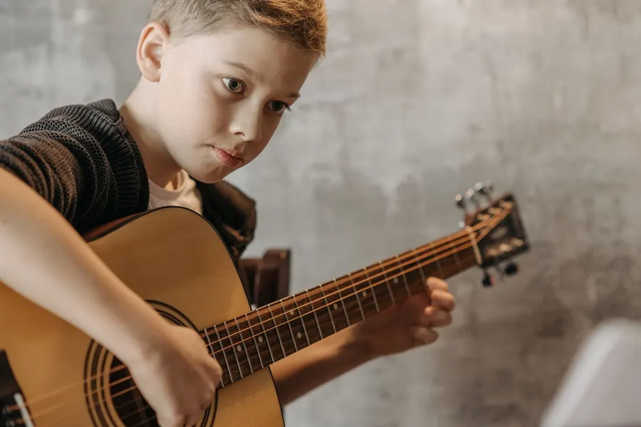 Boy concentrating while playing an acoustic guitar