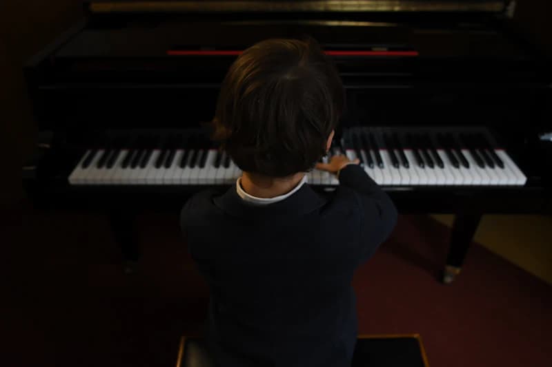 Child playing a grand piano in a dark room