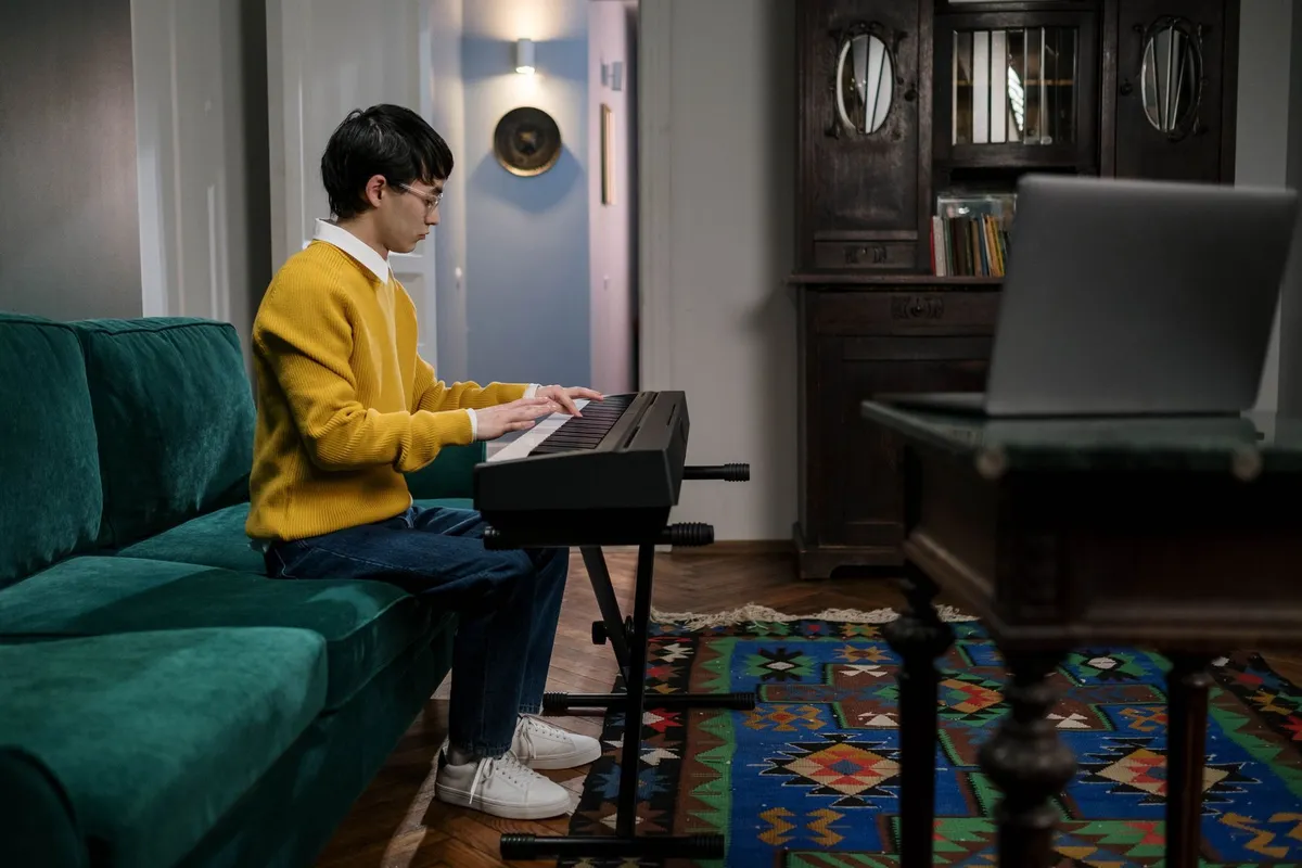 Teenager playing a keyboard with a laptop open beside him for an online lesson