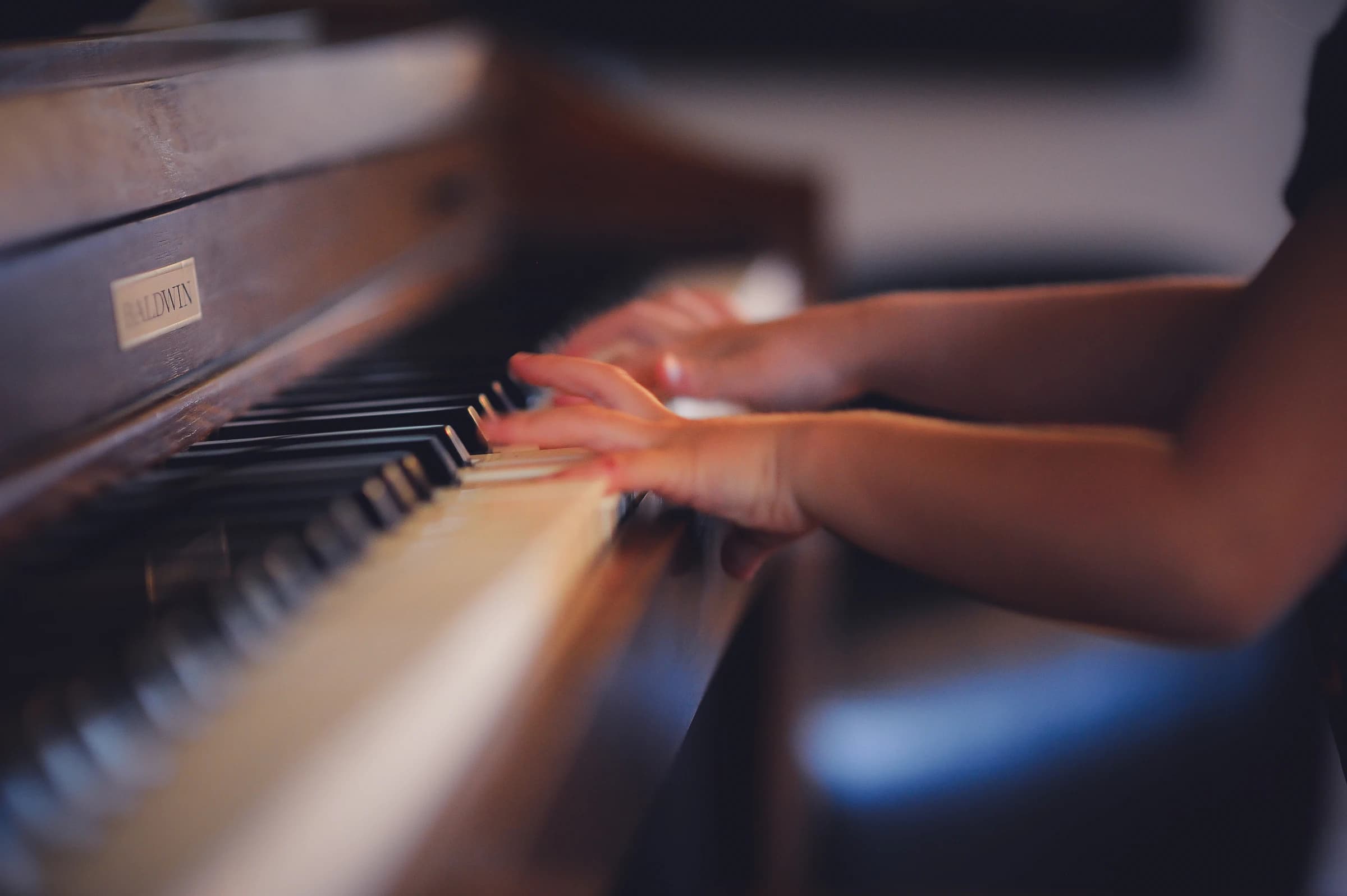 Hands playing an upright piano in warm light